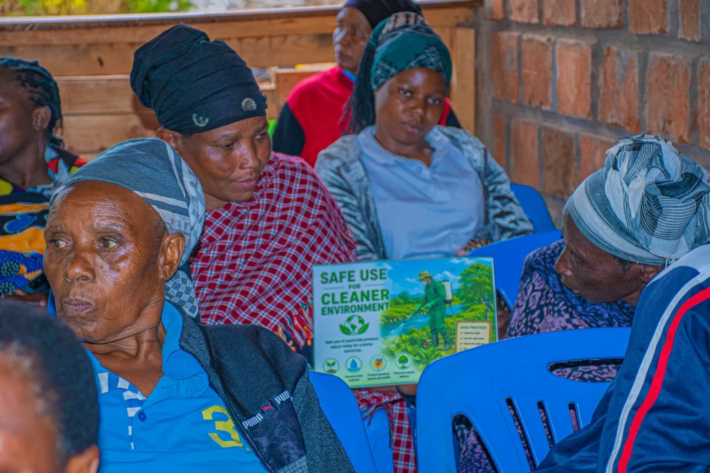 A seated farmer holding the “Safe Use for Cleaner Environment” placard during the training session