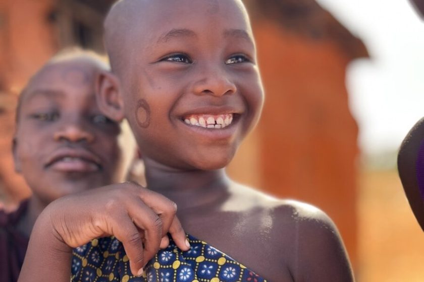 A smiling young child in traditional clothing outdoors attire.